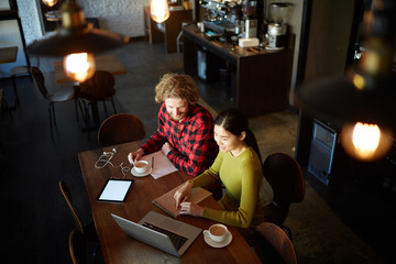 Creative designers sitting by table in cafe and looking for new design ideas in the net