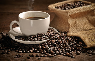 warm cup of coffee with sack inside by coffee bean on wood background