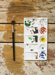 Palette with paints stains and watercolor brush on wooden background.