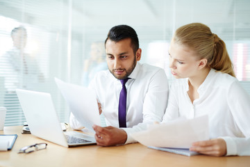 Fototapeta premium Young businessman showing paper to his colleague while working in office