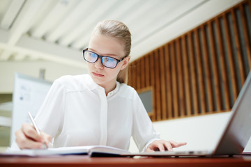 Diligent student or young specialist writing down working plan or financial notes