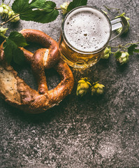 Close up of mug of beer and pretzel with hops on dark rustic background, top view, copy space....