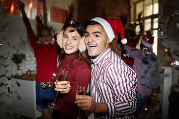 Happy young couple with flutes of champagne celebrating xmas with friends