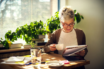 Charming cheerful satisfied middle age short hair woman sitting at the table in the morning at home...