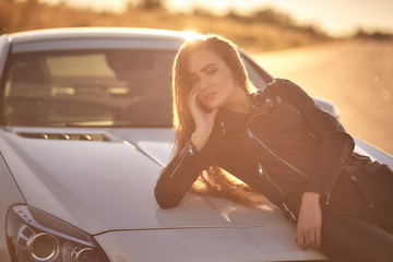 beautiful sexy girl with long hair in a leather jacket and leather pants in sunglasses gets out of the car at sunset