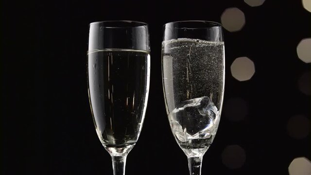 Two flutes of champagne with transparent pieces of ice on the bottom.Bokeh blinking black background. Close up