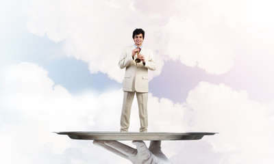 Businessman on metal tray playing fife against blue sky background