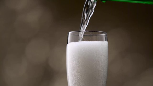 Champagne poured into glass from green bottle. Bokeh background. Close up