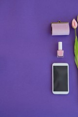 Tulips, purse, nail polish and mobile phone arranged on purple