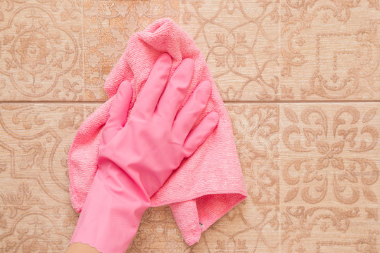 *Employee hand in rubber protective glove with micro fiber cloth washing a ceramic tiles from dust in the bathroom. Spring general or regular clean up. Commercial cleaning company concept. 