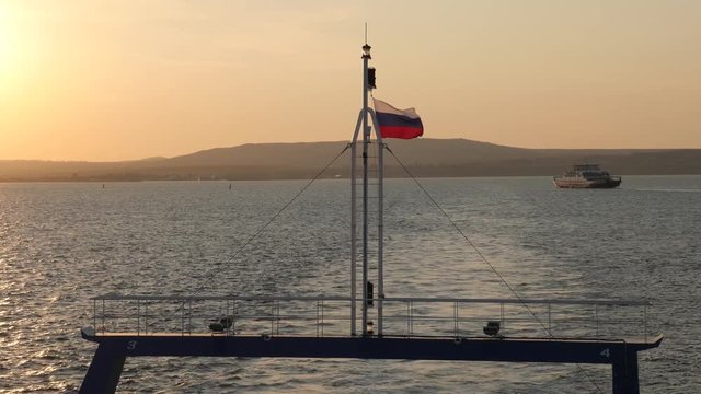 Russian flag fluttering in the wind on the stern of the ship. view from ferry sails through the Strait of Kerch from Crimea to Russia at sunset. seascape with ship traffic