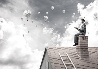 Man on roof reading book and aerostats flying in air