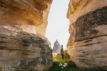 The woman stands between beautiful rocks and admires the landscape in Cappadocia in Turkey. The landscape of Cappadocia. Hills and a passage between them.