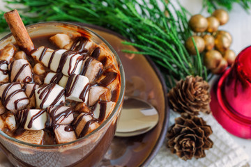 Close up hot chocolate in clear glass topping with marshmallow and dark chocolate sauce on wood table in top view, copy space with Christmas theme decoration background. Concept to present Xmas drink.