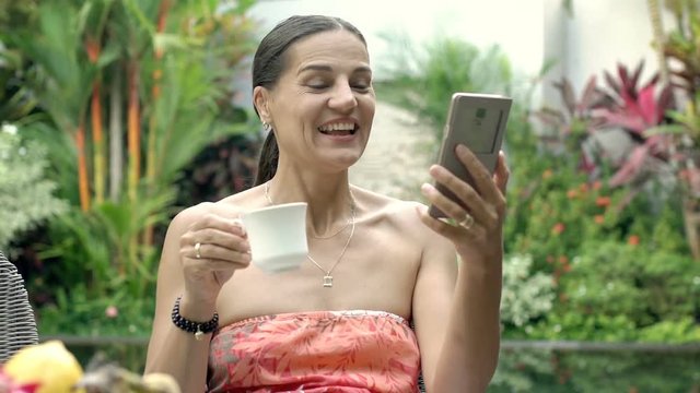Attractive woman drinking coffee and having a videocall on smartphone, steadycam shot
