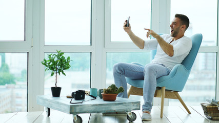 Young happy man have online video chat using digital tablet computer sitting on balcony in modern...