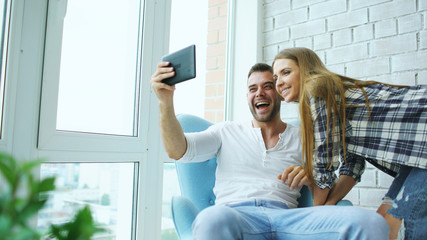 Young attractive couple having online video chat using tablet computer sitting at balcony in modern...