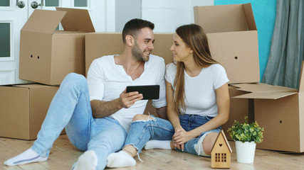 Young couple sitting on floor using tablet computer after reloction in their new home