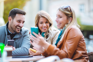 Group of three friends using phone in outdoor cafe on sunny day