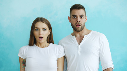 Obraz premium Portrait of young couple actively surprising and wondering looking into camera on blue background
