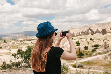 Fototapeta premium A tourist makes a photo on the phone in memory of a beautiful view of the hills in Cappadocia in Turkey. Travel, tourism, vacation.