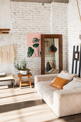 Loft interior with sofa, mirror, wahite brick wall, painting, flowers in pot.