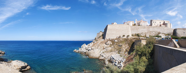 Corsica, 03/09/2017: il Mar Mediterraneo e la spiaggia con vista sullo skyline dell'antica Cittadella di Calvi con le sue antiche mura  - obrazy, fototapety, plakaty