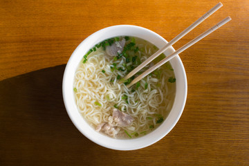 Top view of noodles with meat broth and vegetables in the sunlight