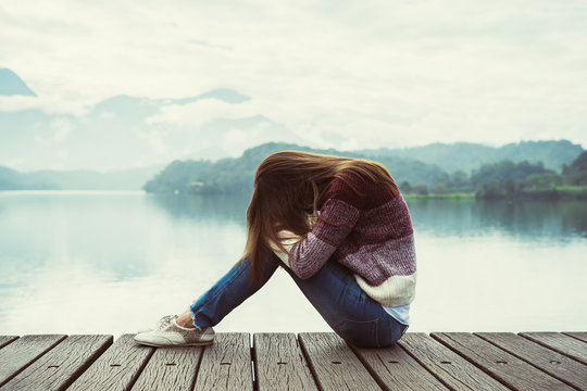 Depressed and stressed woman sitting on wooden pier