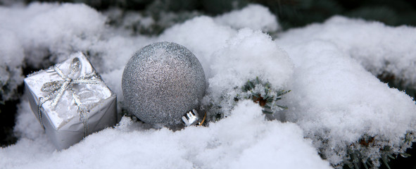 Silver christmas ball and present on white snow.