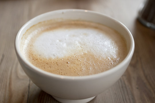 Closeup image of a coffee latte in a white bowl on a wooden table.