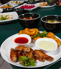 snacks to beer. cheese balls, chicken wings, onion rings, sauce and dishes with different food on the table
