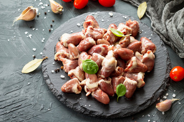 Raw livers on a slate board, cherry tomatoes and spices on a gray stone stone background. Copy space.