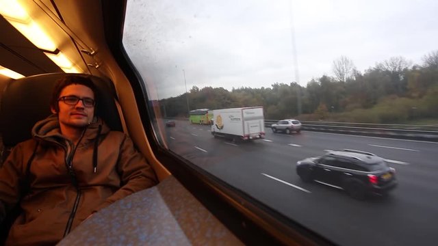The man in glasses is riding a train along the cars road and smiling