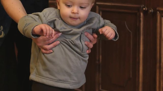 First steps of cute baby boy with mother hands support indoors