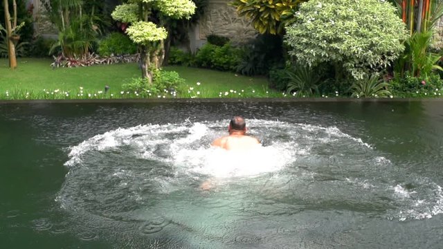 Man swimming in the pool and splashing the water, steadycam shot, slow motion shot at 240fps
