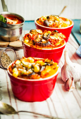 Portioned casserole.from corn grits and vegetables in tomato sauce in red ceramic baking molds. Vegan holiday christmas dinner. Healthy lifestyle and plant-based food concept.