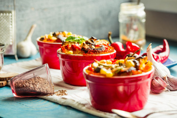 Portioned casserole.from corn grits and vegetables in tomato sauce in red ceramic baking molds. Vegan holiday christmas dinner