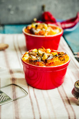 Portioned casserole.from corn grits and vegetables in tomato sauce in red ceramic baking molds. Vegan holiday christmas dinner. Selective focus.