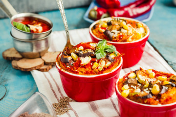 Portioned casserole.from corn grits and vegetables in tomato sauce in red ceramic baking molds. Vegan holiday christmas dinner.