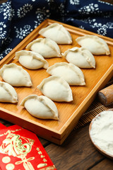 Fototapeta na wymiar raw dumplings on wooden plate with flour and rolling pin and red packet,Chinese word translation:happiness