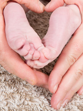 young couple's hands form a heart around the newborn baby's feet