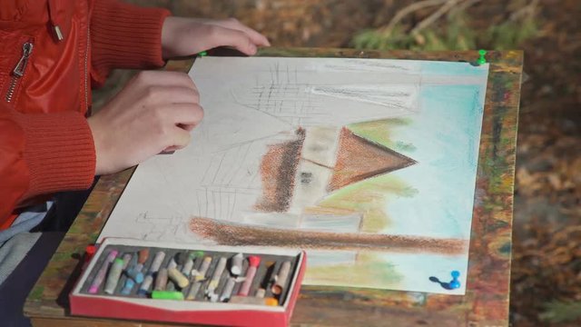 Concept teacher of drawing and a student: close-up, in the frame only adult and child's hand. Child draws pastel crayons in the nature (a picture on grass), and teacher helps to make the feathering.