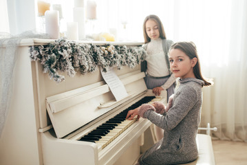 Two pretty sisters sitting at white fortnpiano