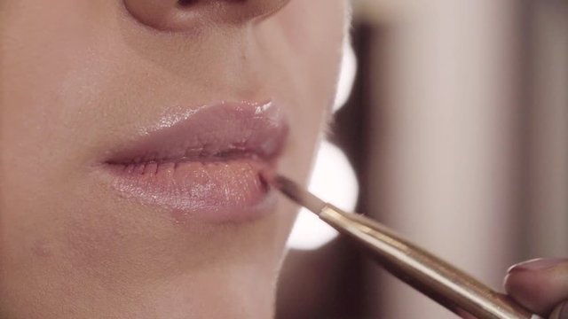 Extreme close up of the female lips. Professional makeup artist applying color lip gloss on the model's lips