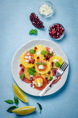 Orange pomegranate goat cheese salad on light blue background. Top view, space for text.