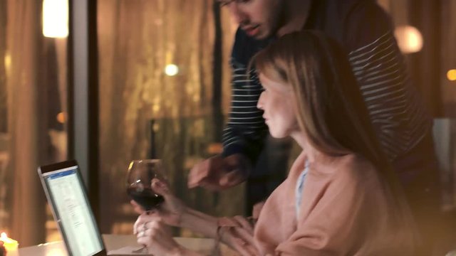 Beautiful woman working on laptop and talking with young man on evening veranda