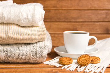 Stack of cozy knitted warm sweater , wooden background . Sweaters in retro Style and a Cup of hot chocolate. The concept of warmth and comfort.