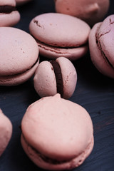 Making homemade French Macarons with raspberry coffee flavor: Close up of imperfect, light pink macarons filled with chocolate ganache on black wooden background