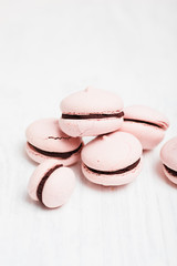 Making homemade French Macarons with raspberry coffee flavor: Close up of imperfect, light pink macarons filled with chocolate ganache on white wooden background